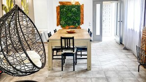 Een eetruimte met een houten tafel, stoelen, een hangstoel, een groene wandpaneel en een vloerkleed.