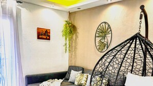 Een moderne woonkamer met een grijze bank, een hangstoel, een klein rond tafeltje en een geweven vloerkleed.