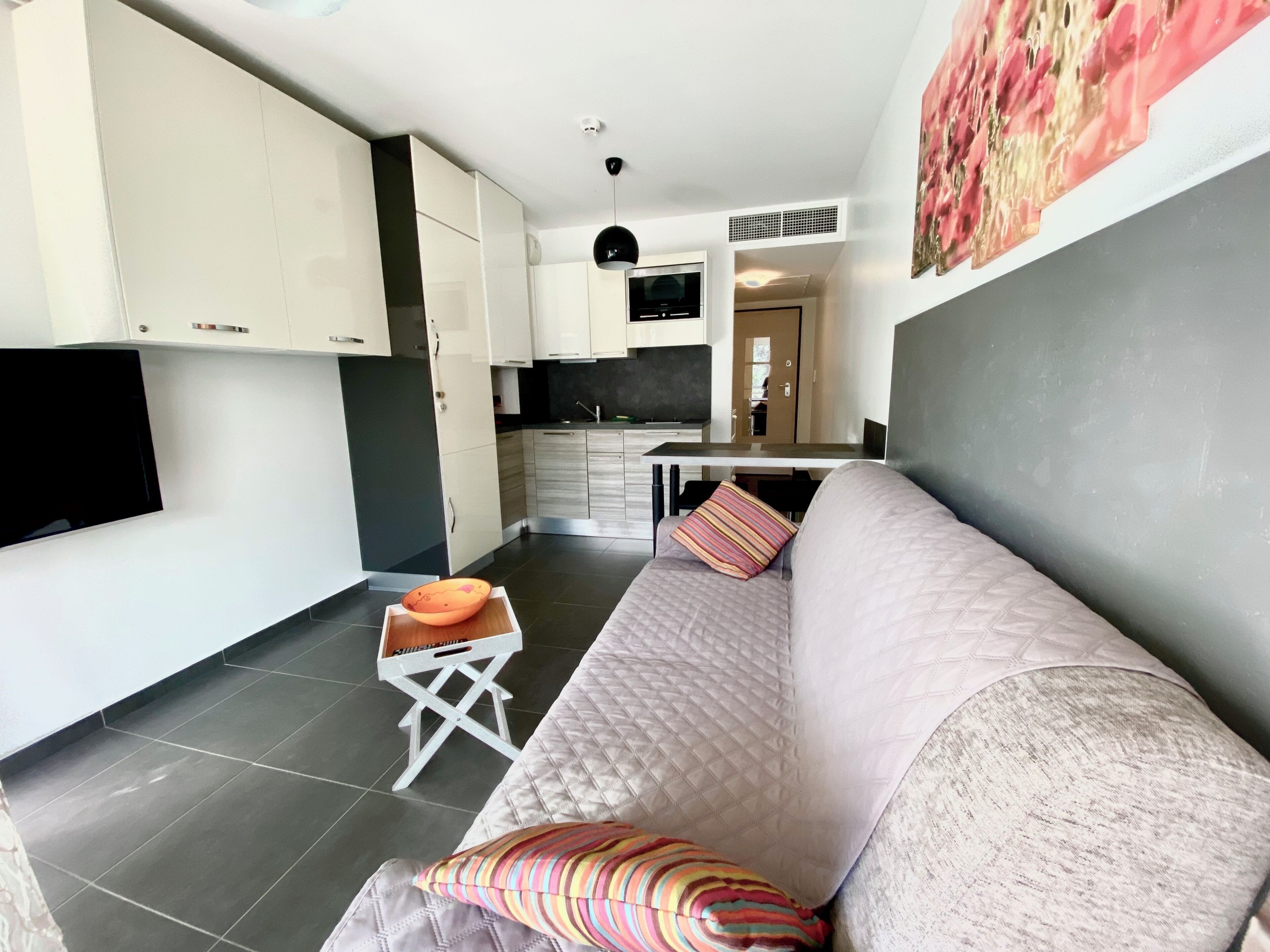 A modern living room with a sofa, a small table with a bowl, and a kitchen area in the background.