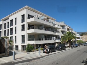Um edifício com vários andares, varandas, área de estacionamento e céu claro.