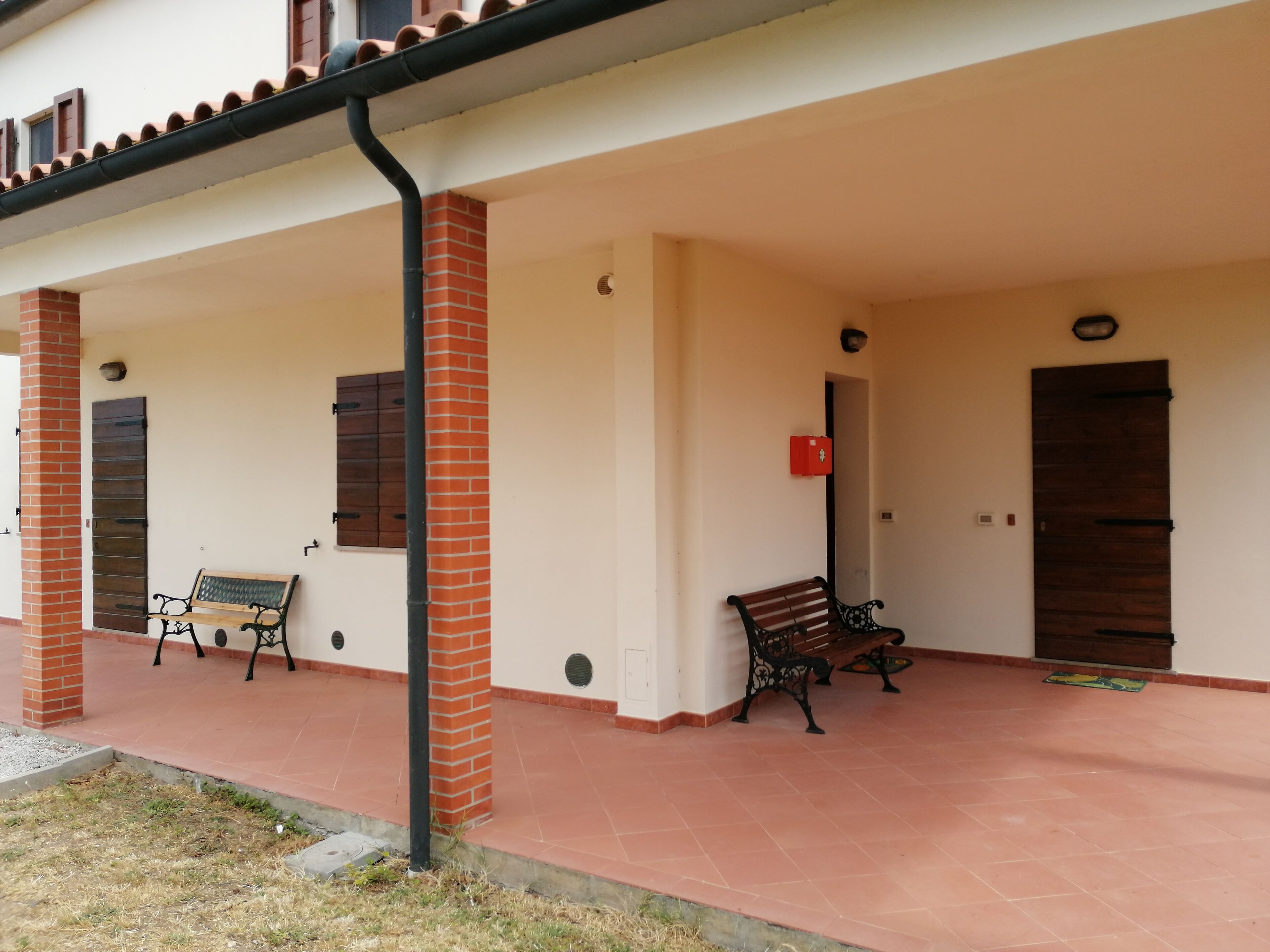 A covered outdoor area with two benches, a red mailbox, and a door.