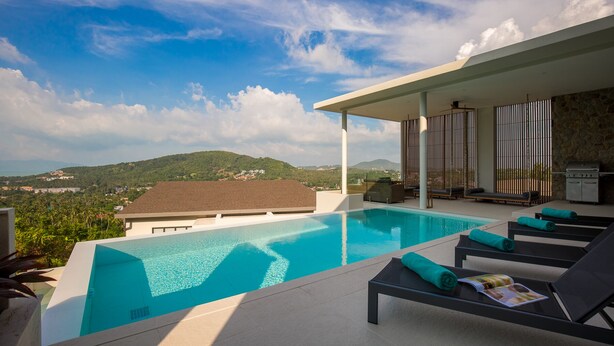 A modern outdoor pool area with a clear view of the surrounding landscape, including hills and a distant town. - Baan Ouyan 5-bed luxury family home on Bophut Hill (Ko Samui)