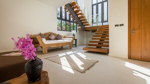 A modern living room with a wooden staircase, a sofa, and a vase of flowers. - Baan Ouyan 5-bed luxury family home on Bophut Hill (Ko Samui)