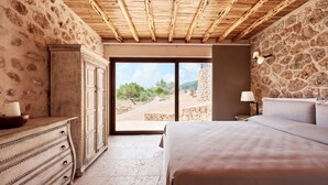 Een slaapkamer met een stenen muur, houten plafond, een bed, een dressoir en uitzicht op de omgeving.