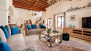 Een ruime woonkamer met hoog houten plafond, een trap en een grote televisie op een houten kast.