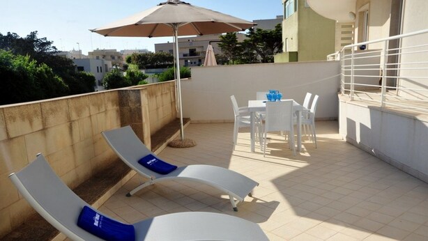 Une terrasse sur le toit avec deux chaises longues blanches, une table avec des chaises et un grand parasol.