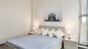 Une chambre à coucher comprenant un lit, deux tables de chevet avec des lampes, une œuvre d’art accrochée au mur et une fenêtre avec des rideaux.