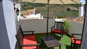 Ein Balkon mit Tisch und Stühlen, einem Blumentopf und Blick auf Weinberge.