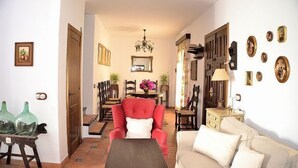 Ein Wohnzimmer mit einem roten Sessel, einem beigen Sofa, einem Holztisch und einem Essbereich mit Tisch und Stühlen.