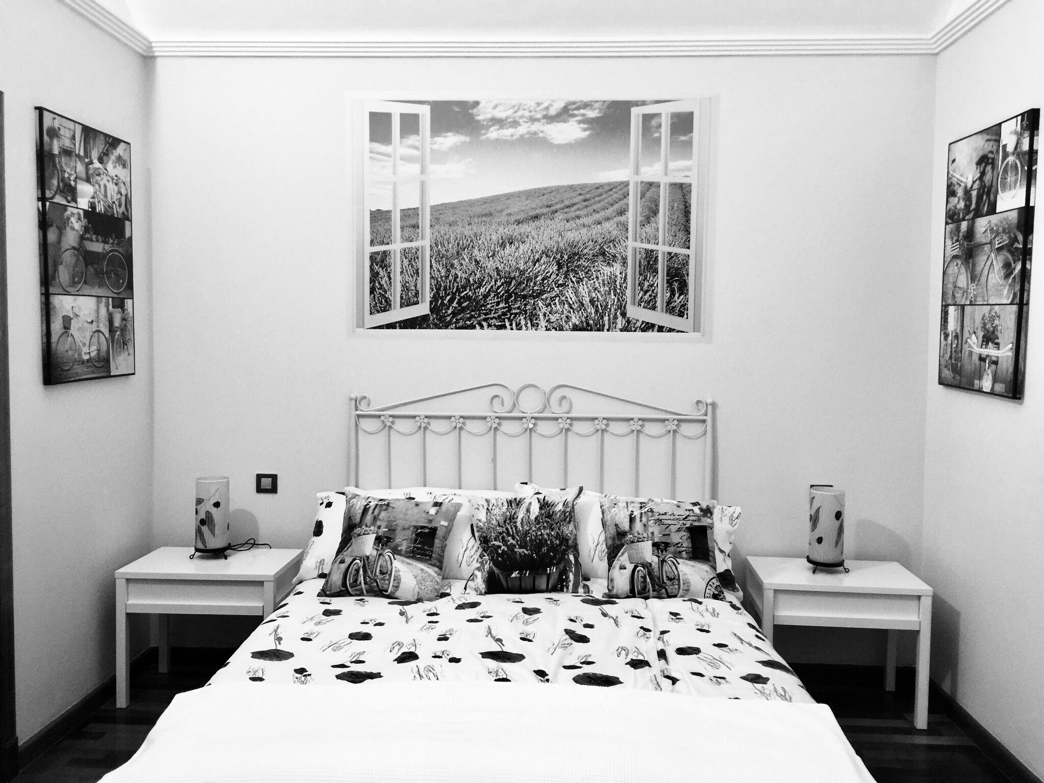 A bedroom with a bed, two bedside tables, and a large window with an open view of a field.