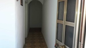 Un couloir étroit, recouvert d’un tapis à motifs, une porte avec un panneau de verre et un petit tableau encadré accroché au mur.