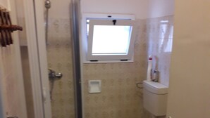 Une petite salle de bain avec une douche, des toilettes et une fenêtre située au-dessus des toilettes.