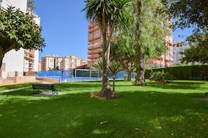 Un patio cuidado con un banco, palmeras y una cerca azul.