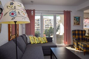 Una sala de estar con un sofá, una mesa, una lámpara, una silla y vistas a una zona residencial a través de un ventanal.