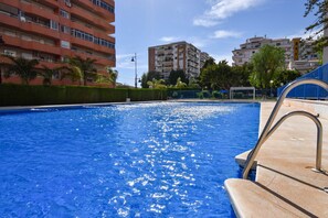 A swimming pool with clear blue water, surrounded by a low hedge and a metal fence.