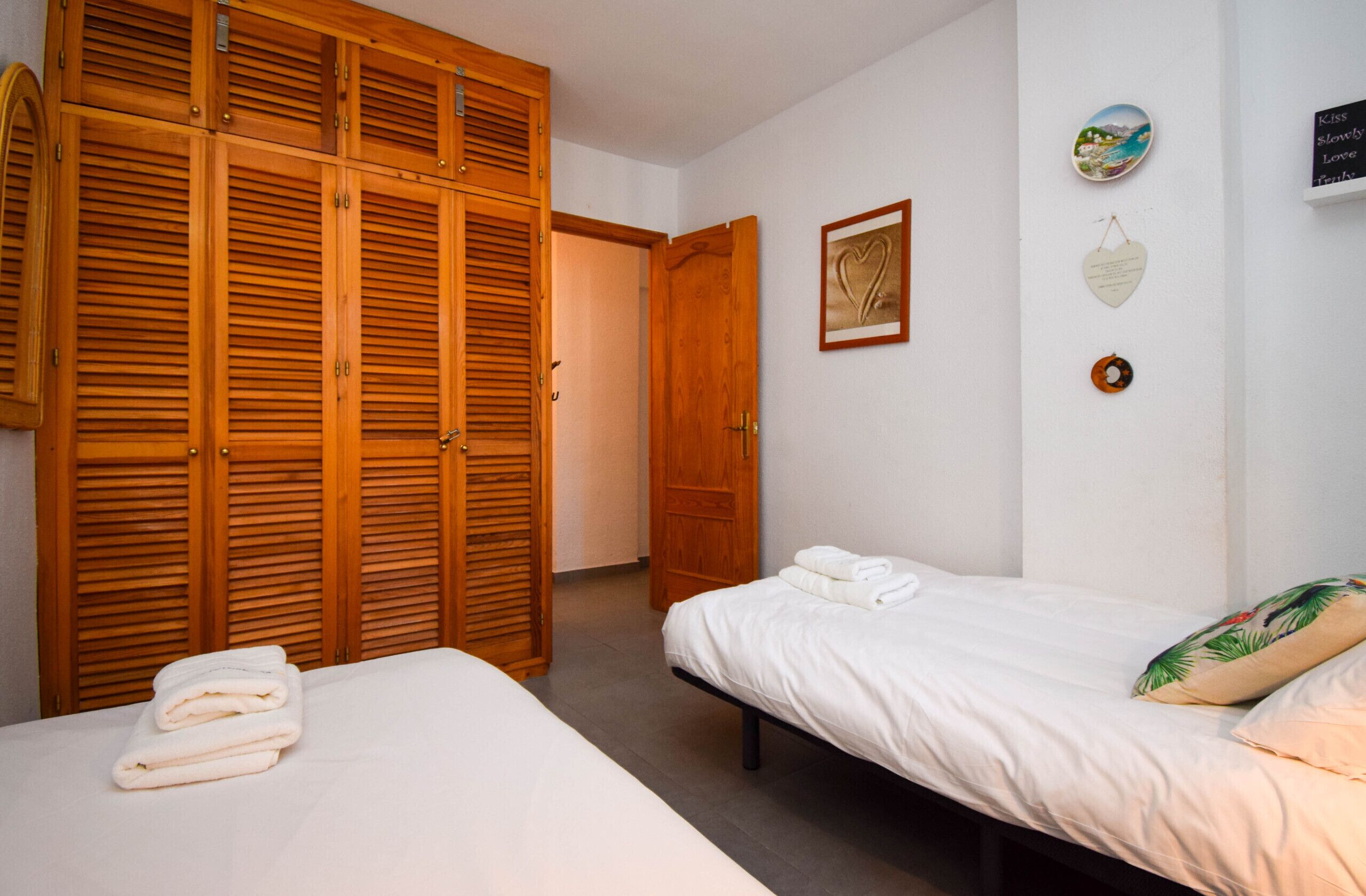 A bedroom with two beds, wooden wardrobes, and a door leading to another room.