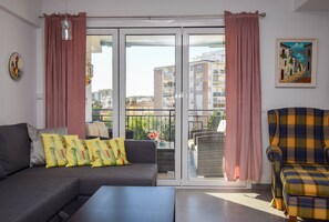 A modern living room with a sofa, armchair, and a balcony with curtains.