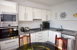 Una cocina moderna con armarios blancos, electrodomésticos de acero inoxidable, encimera de granito y una mesa de comedor con sillas.