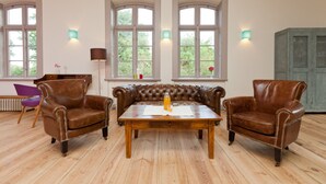 A room with a leather sofa set, a wooden coffee table, and two leather armchairs. There are large windows with white frames and green wall sconces. - Spacious and stylish in the monument to the Müritz, near the lake and golf course (Lexow)