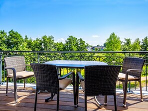 A balcony with wicker chairs and a table, overlooking a green landscape with houses in the distance.