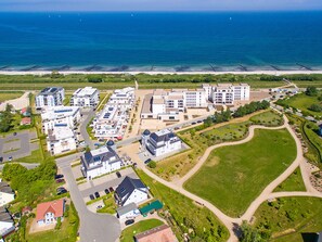 An aerial view of a coastal residential area with modern buildings, a beach, and a marina.