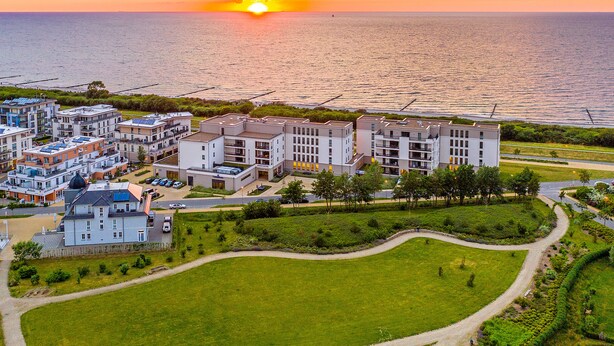 A coastal residential area with modern apartment buildings, a marina, and a sunset view. - Comfortable large suite, pool and sauna, 30 meters to the beach, large south-facing balcony (Börgerende)