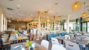 A modern restaurant with wooden tables, blue and white chairs, and pendant lighting. - Comfortable large suite, pool and sauna, 30 meters to the beach, large south-facing balcony (Börgerende)