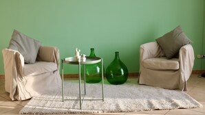A living room with two beige armchairs, a round table with two green vases, and a white rug.