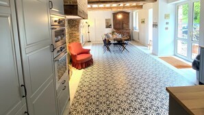 A kitchen with white cabinets, a red chair, a patterned floor, and exposed wooden beams.