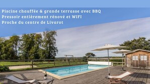 A swimming pool with wooden deck chairs and umbrellas, a wooden cabin, and a view of the countryside.