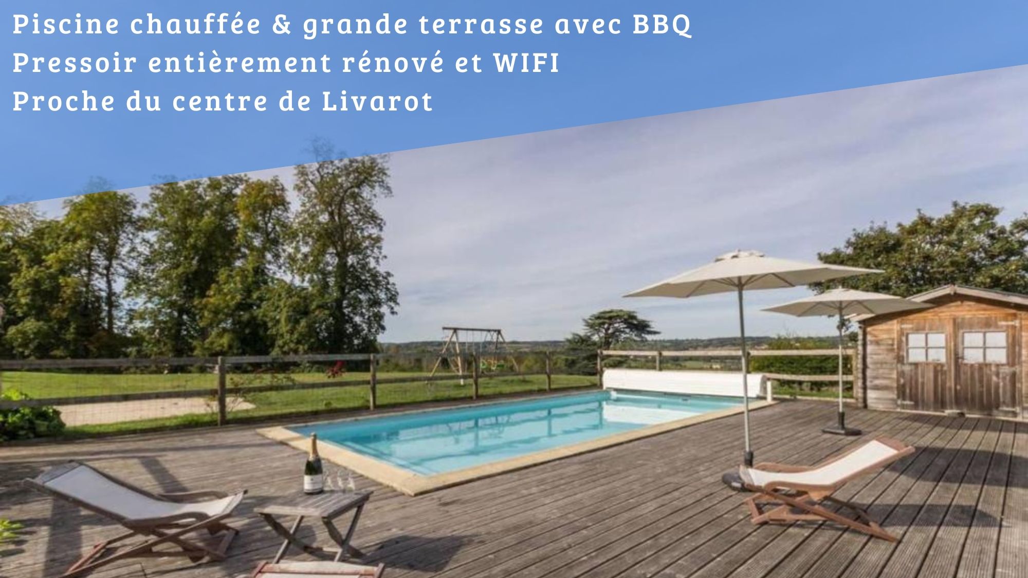 A swimming pool with wooden deck chairs and umbrellas, a wooden cabin, and a view of the countryside.