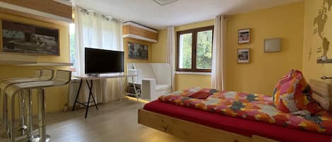 Um quarto com uma cama, uma escrivaninha, uma televisão e uma janela.