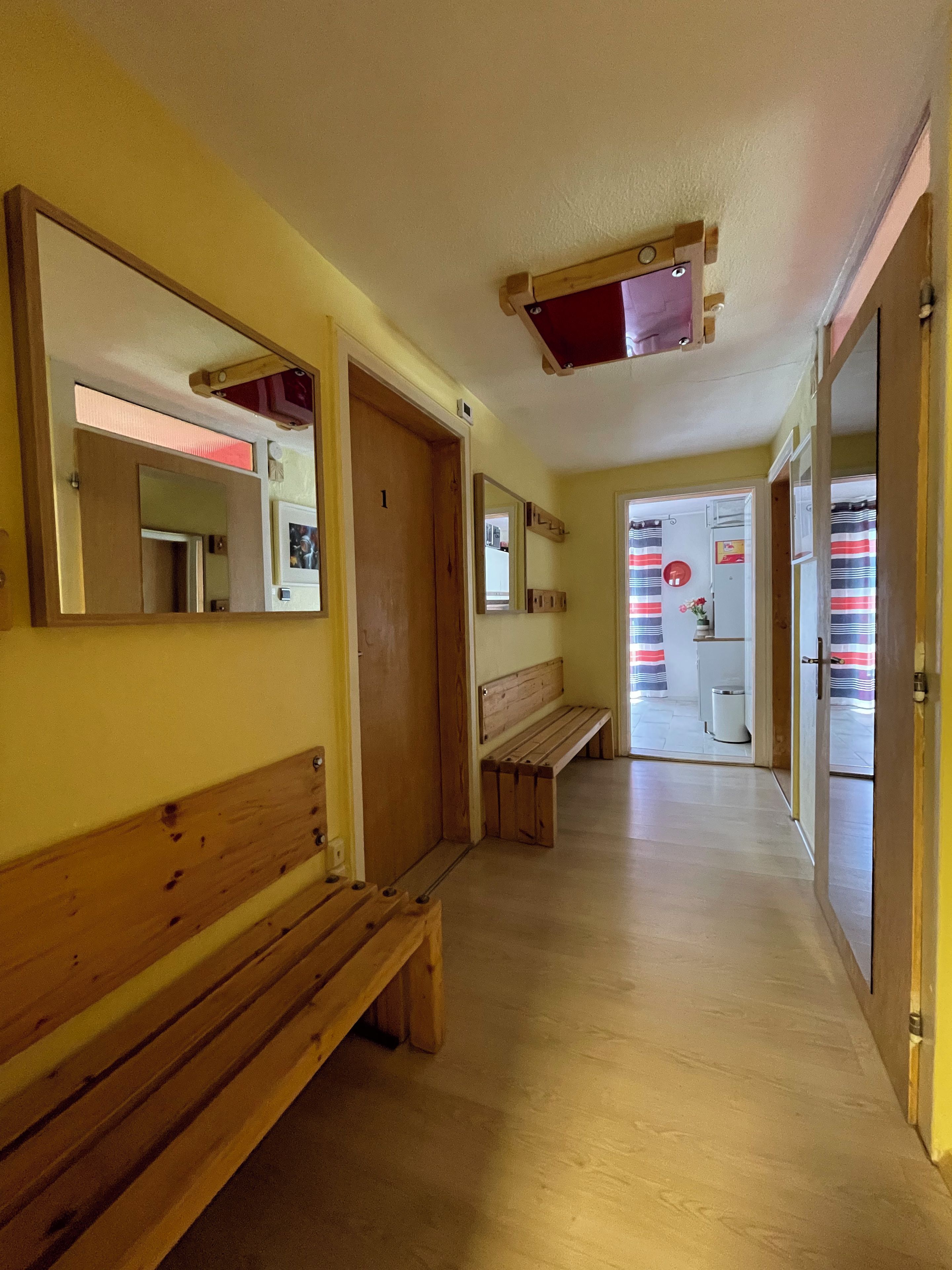 Ein Korridor mit hölzernen Bänken, einer Tür mit einer Nummer und einem Spiegel an der Wand.