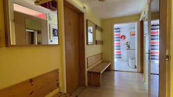 Ein Korridor mit hölzernen Bänken, einer Tür mit einer Nummer und einem Spiegel an der Wand.