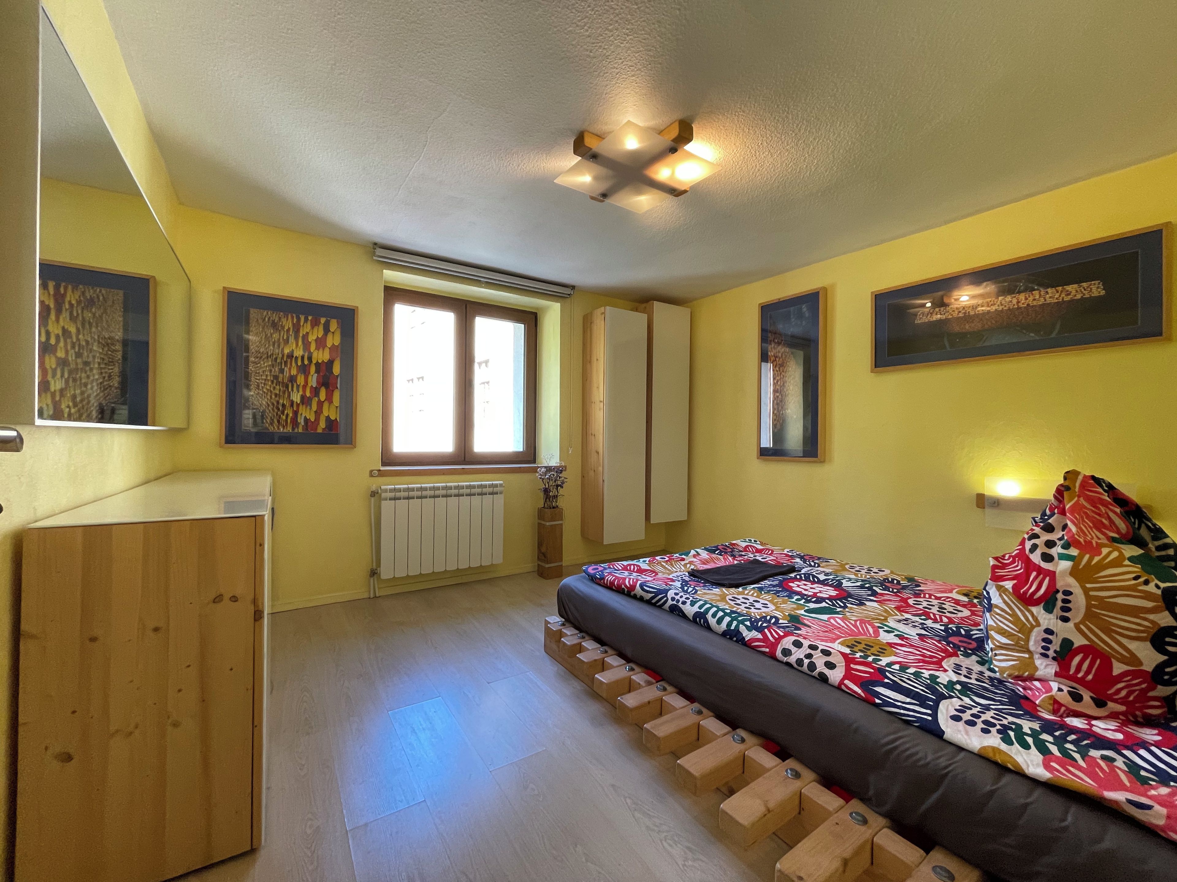 A bedroom with a bed, a wardrobe, a radiator, and a window.