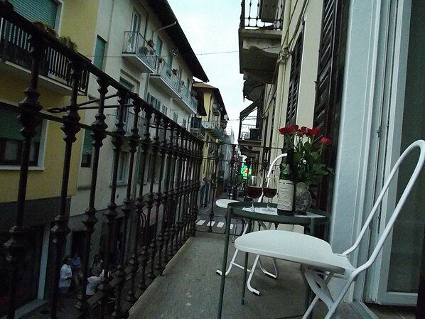 A narrow outdoor corridor with a metal fence, a small table with chairs, and a vase with flowers.