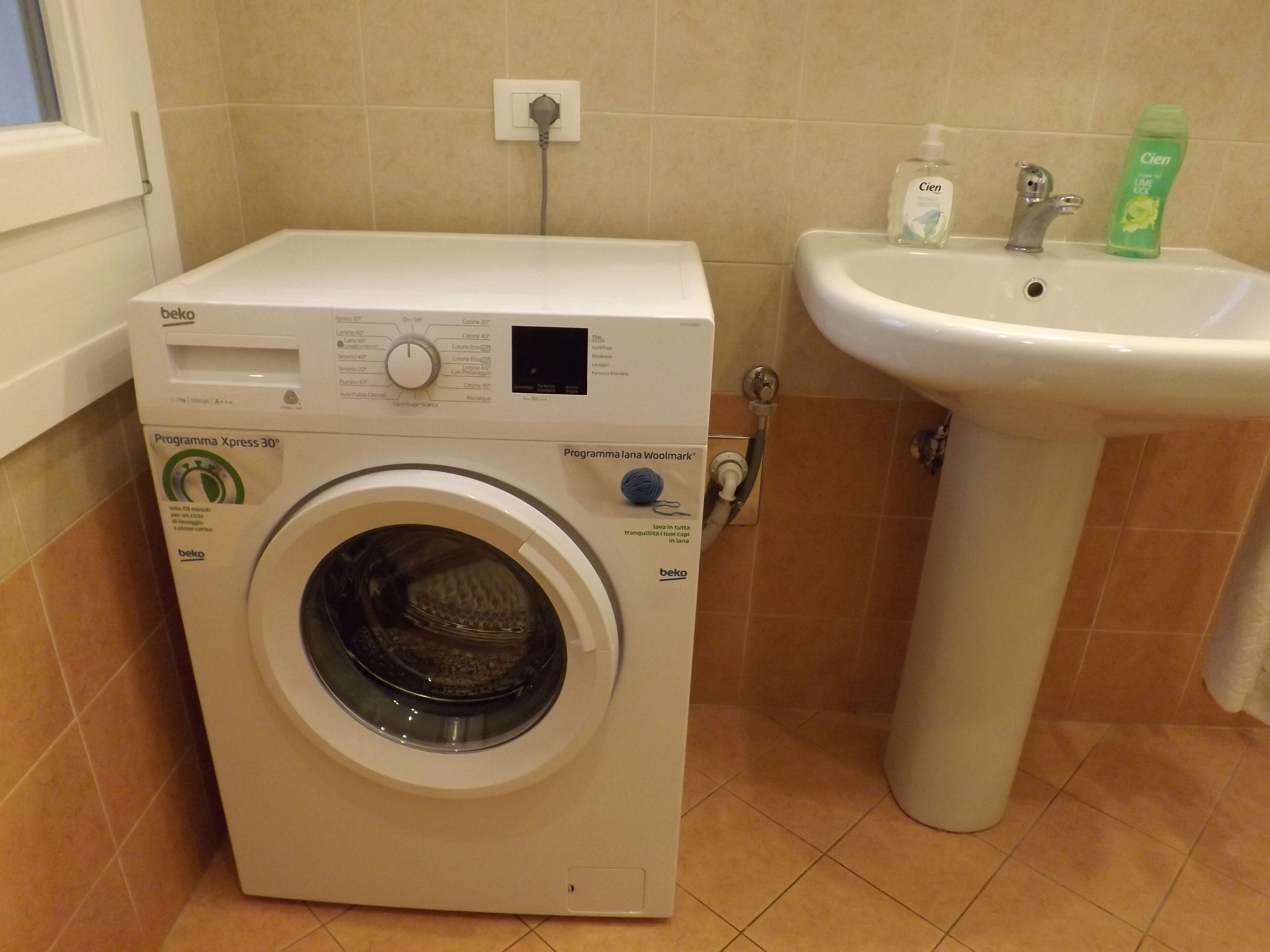 Lavadora compacta con panel de control, lavabo y artículos de aseo.