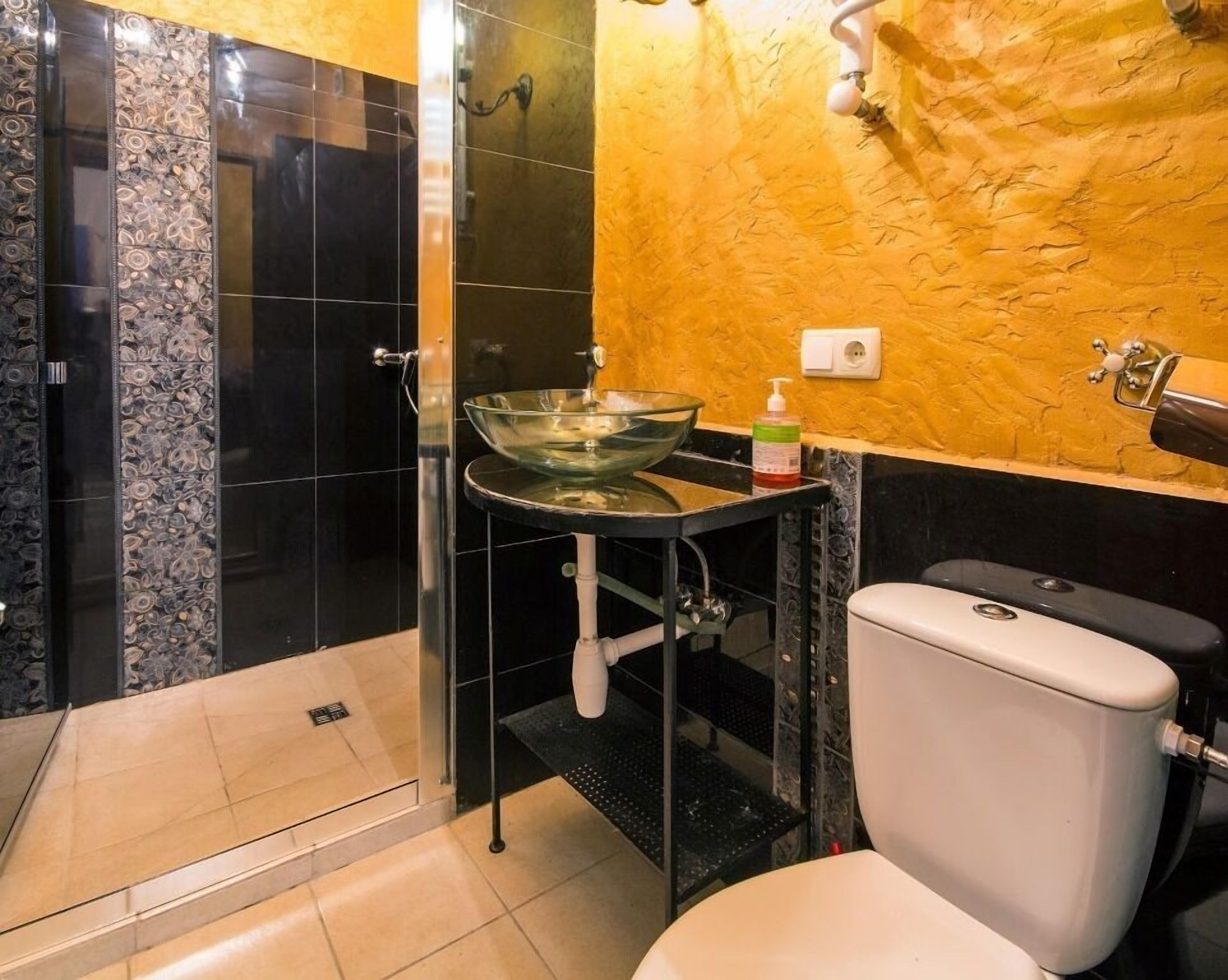 Et badeværelse med vask i glas, toilet og bruseområde.