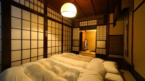 Una habitación tradicional japonesa con suelo de tatami, techo de madera bajo y puertas correderas.