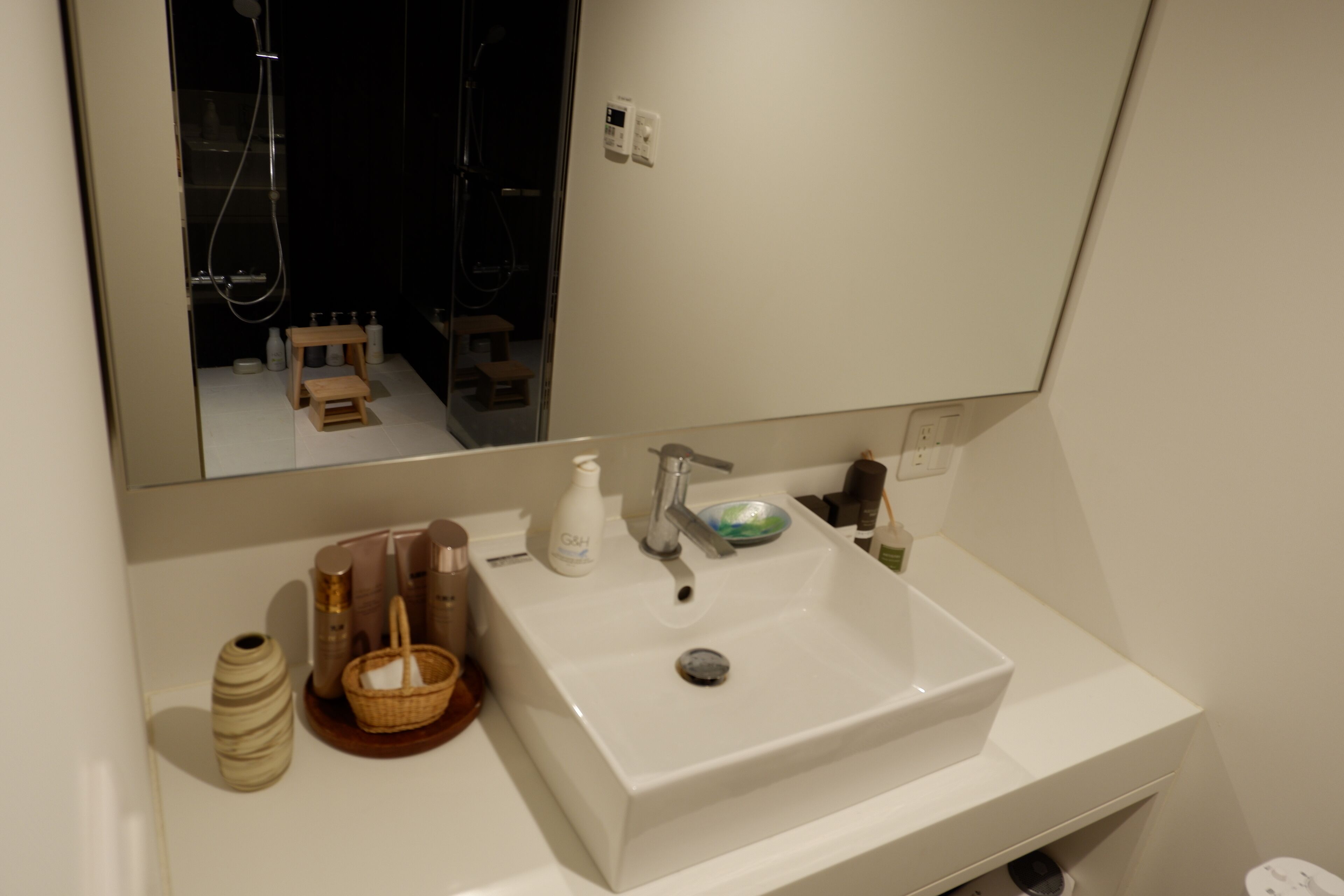 A bathroom with a white sink, mirror, and a small wooden stool.