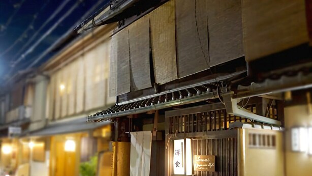 Un edificio japonés tradicional con fachada de madera, entrada de tejas y un letrero que indica un restaurante.