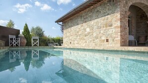 A clear swimming pool with stone walls and a covered seating area. - Villa Ventotto by Paola Orazioli (Arezzo)