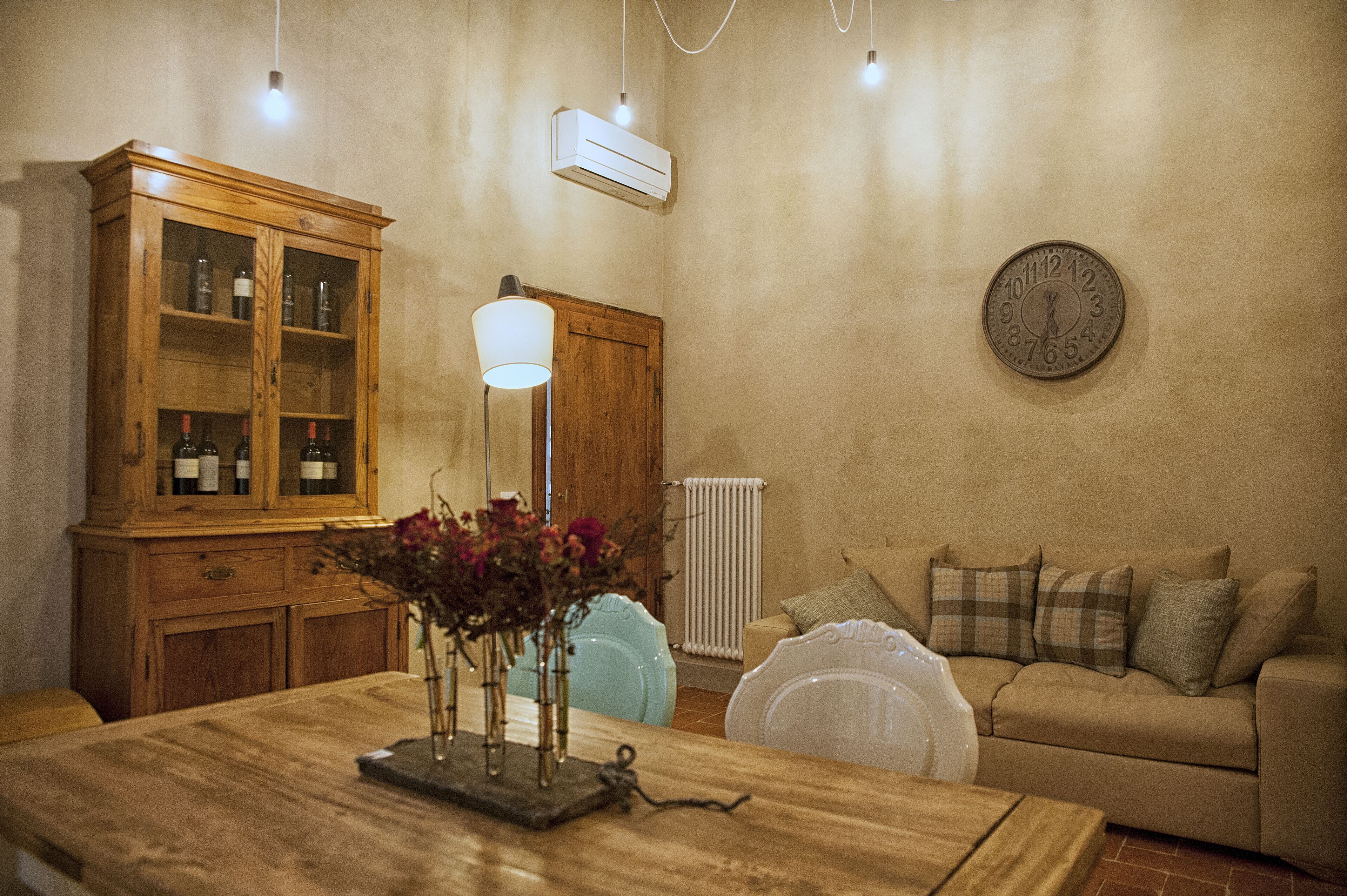 A living room with a wooden cabinet, a table with a vase, a clock on the wall, and a sofa.