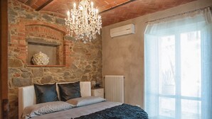 A bedroom with a stone wall, a chandelier, a radiator, and a window with curtains. - Villa Ventotto by Paola Orazioli (Arezzo)