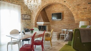 A dining area with a brick wall, a chandelier, and a flat-screen TV mounted above a fireplace. - Villa Ventotto by Paola Orazioli (Arezzo)