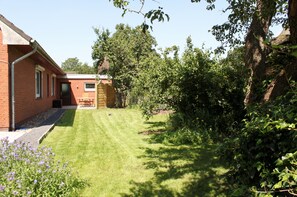 A well-maintained lawn with a brick building, a wooden bench, and a tree in the background. - Quiet location and yet right in the middle (Risum-Lindholm)