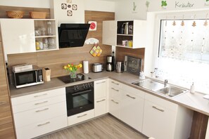 A modern kitchen with white cabinets, a microwave, stove, and a sink. - Quiet location and yet right in the middle (Risum-Lindholm)