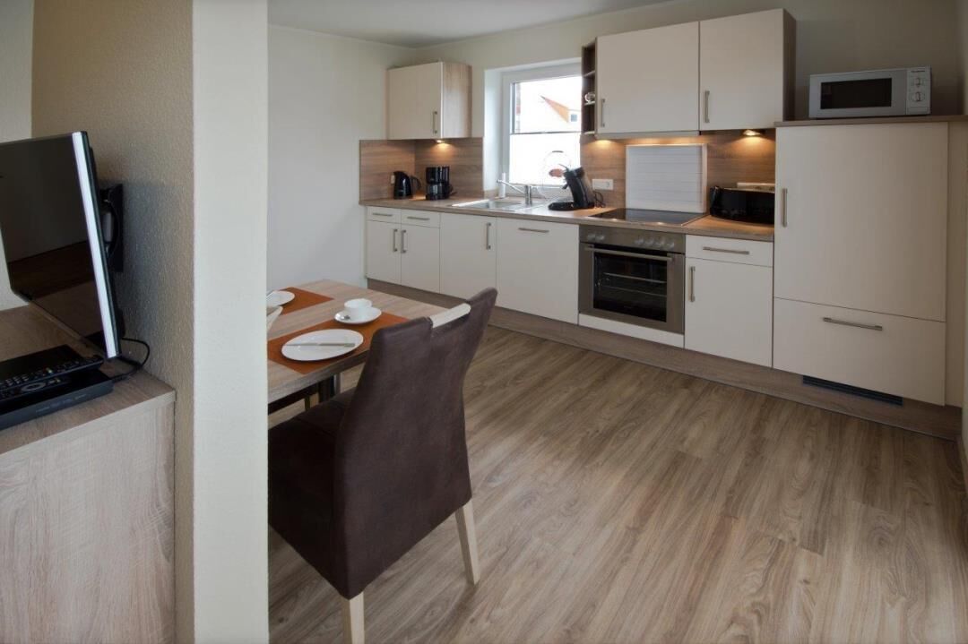 A modern kitchen with white cabinets, a microwave, a coffee maker, and a dining area with a table and chairs.
