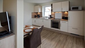Een moderne keuken met witte kastjes, een magnetron, een koffiezetapparaat en een eethoek met een tafel en stoelen.