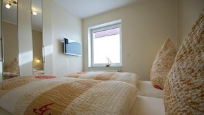 Een slaapkamer met twee bedden, een grote spiegel, een raam met uitzicht op een zeilboot en een klein plankje met een decoratief object.